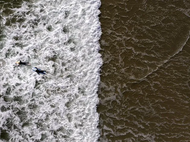 In this photo taken with a drone, two surfers wade through water in Huntington Beach, Calif., Monday, April 17, 2023. (Photo by Jae C. Hong/AP Photo)
