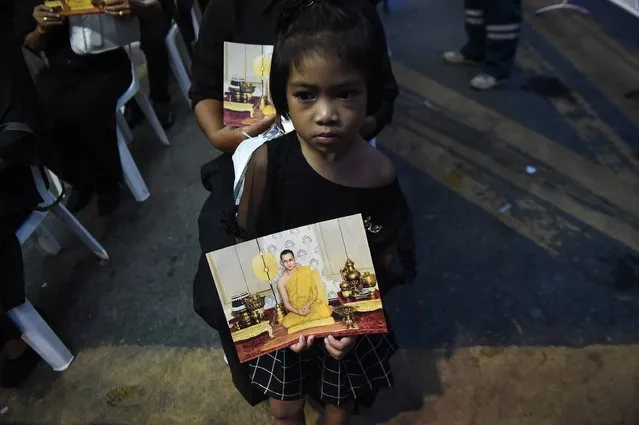 A girl dressed in black holds an image of the late Thai King Bhumibol Adulyadej, while waiting to enter the Grand Palace to pay respects, in Bangkok on October 29, 2016. Thousands of Thais streamed into the gates of Bangkok's Grand Palace on Saturday as the public was granted its first chance to enter the throne hall where the body of late King Bhumibol Adulyadej is lying in state. (Photo by Lillian Suwanrumpha/AFP Photo)