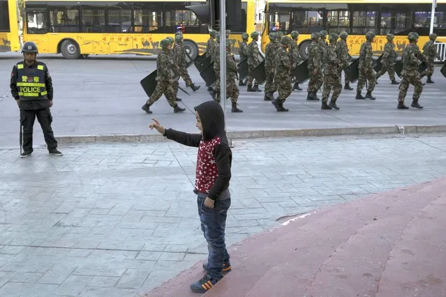 In this November 5, 2017, file photo, a child reacts as security personnel march by in a show of force in Kashgar in western China's Xinjiang region. A Chinese Communist Party official signaled Monday, Dec. 21, 2020 that there would likely be no let-up in its crackdown in the Xinjiang region, but said the government's focus is shifting more to addressing the roots of extremism. (Photo by Ng Han Guan/AP Photo/File)