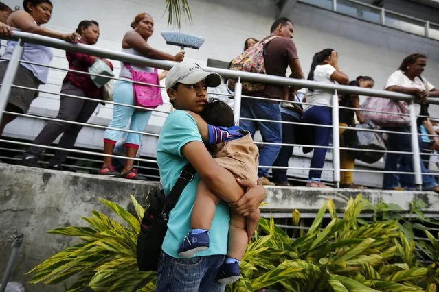 A boy carries her young brother as people line up outside a supermarket in Caracas January 19, 2015. (Photo by Jorge Silva/Reuters)