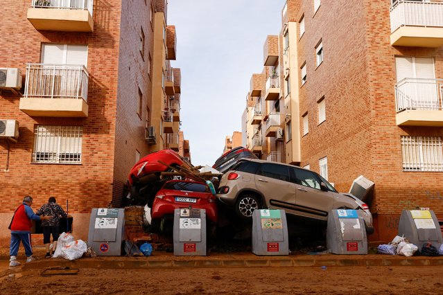People walk next to piled-up cars after heavy rains in Alfafar, in Valencia, Spain, on November 1, 2024. (Photo by Susana Vera/Reuters)