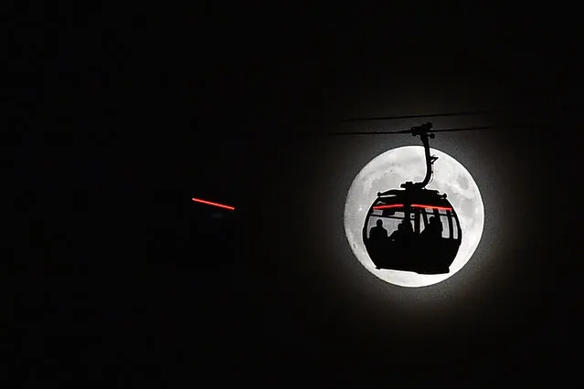 The moon rises behind a car on the The Emirates Air Line (cable car) in London's Docklands on November 13, 2016. Tomorrow, the moon will orbit closer to the earth than at any time since 1948, named a “supermoon”, it is defined by a Full or New moon coinciding with the moon's closest approach to the Earth. (Photo by Glyn Kirk/AFP Photo)