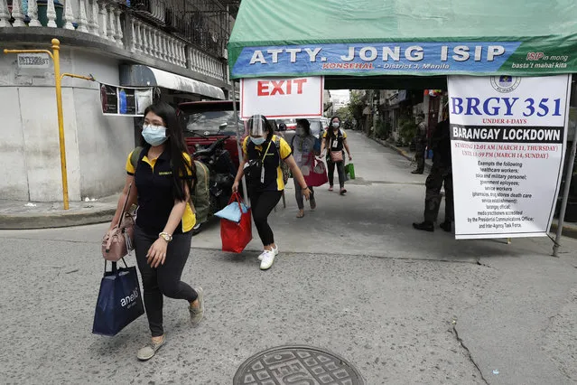 Residents wearing protective masks carry belongings outside a village that was placed under lockdown due to the number of COVID-19 cases among residents in Manila, Philippines on Thursday, March 11, 2021. The Philippine capital placed two villages and two hotels on lockdown Thursday and police have renewed warnings against kissing and other “public display of affection” after a new surge in coronavirus infections. (Photo by Aaron Favila/AP Photo)
