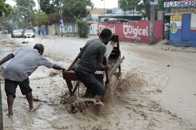 Men work to keep a vendor's stand afloat on a street flooded during a heavy rain, in Port-au-Prince, Haiti, Saturday, June 3, 2023. (Photo by Joseph Odelyn/AP Photo)
