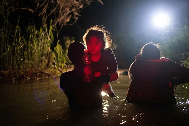 Child migrant Eliana, 4, from Guatemala, is carried towards a member of the Texas Army National Guard, after she and other asylum-seeking migrants waded across the Rio Grande river into the United States from Mexico in Roma, Texas, U.S., May 13, 2022. (Photo by Adrees Latif/Reuters)
