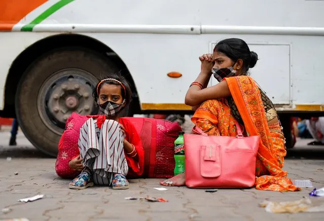 A migrant worker's family sits next to a bus at a bus station, as they wait to return to their village, after Delhi government ordered a six-day lockdown to limit the spread of the coronavirus disease (COVID-19), in Ghaziabad on the outskirts of New Delhi, India, April 20, 2021. (Photo by Adnan Abidi/Reuters)
