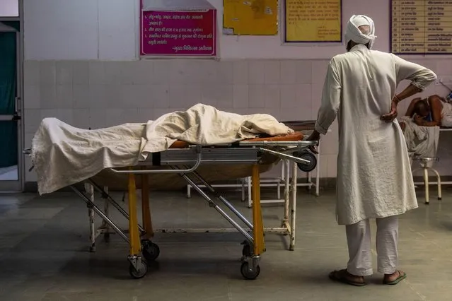 A man stands next to the body of his wife, who died due to breathing difficulties, inside an emergency ward of a government-run hospital, amidst the coronavirus disease (COVID-19) pandemic, in Bijnor, Uttar Pradesh, India, May 11, 2021. (Photo by Danish Siddiqui/Reuters)