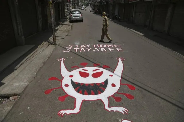 An Indian police man walks past an awareness message painted on a road during a curfew to curb the spread of coronavirus in Jammu, India, Wednesday, May 19, 2021. India has the second-highest coronavirus caseload after the U.S. with more than 25 million confirmed infections. (Photo by Channi Anand/AP Photo)