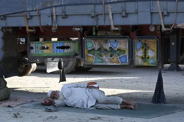 In this picture taken on on September 11, 2023, a truck driver takes a nap next to a truck parked along a road near the Pakistan-Afghanistan border in Torkham, after the Torkham border closed on September 6, 2023, following clashes between border forces of both countries. A gun battle erupted on September 6 between Pakistan and Afghan border forces, officials said, shutting the busiest trade crossing between the two South Asian countries. (Photo by Abdul Majeed/AFP Photo)