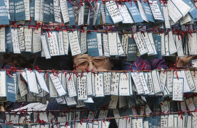 A mother ties a note to a line for good luck in her child's success in an upcoming college entrance exam at Jogye Temple in Seoul, South Korea, Wednesday, November 14, 2018. About 600,000 students high school seniors and graduates across the country are expected to take the state-administrated scholastic aptitude test on Nov. 15. (Photo by Ahn Young-joon/AP Photo)