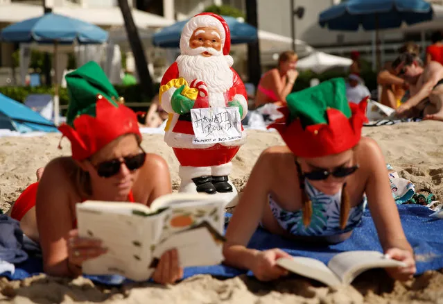 A Santa Claus is perched upon the sand as women in elf hats read on Waikiki Beach on Christmas Day in Honolulu, Hawaii, U.S. December 25, 2016. (Photo by Kevin Lamarque/Reuters)