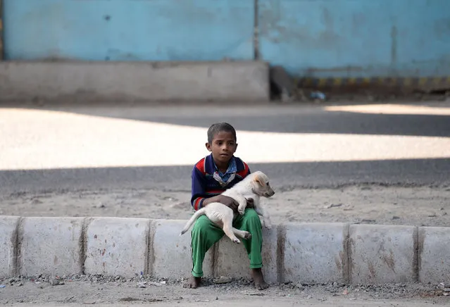An Indian child holds a puppy as he sits on a road divider in New Delhi on December 5, 2016. (Photo by Sajjad Hussain/AFP Photo)