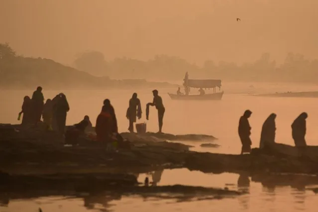 A boatman steers his boat as people stand on the banks on the Narmada River on foggy morning in Jabalpur on November 18, 2023. (Photo by Uma Shankar Mishra/AFP Photo)