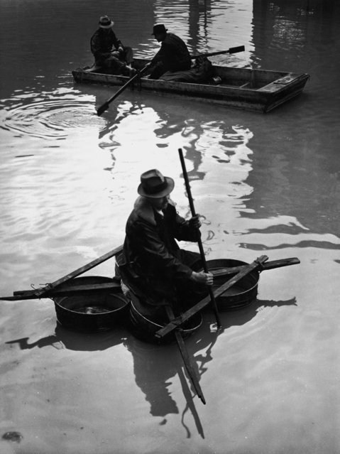 The victim of a flood paddles a makeshift boat fashioned out of four washtubs lashed together with wooden slats, while in the background, two men row a flat boat during a flooding of the Mississippi River, Louisville, Kentucky, February 1937. (Photo by Margaret Bourke-White/The LIFE Picture Collection/Getty Images)