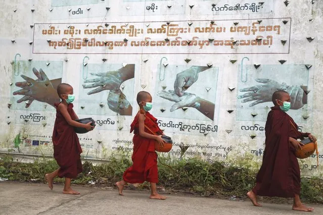 Buddhist novice monks wearing face mask walk past signboard of COVID-19 awareness as they collect morning alms Thursday, July 15, 2021, in Yangon, Myanmar. (Photo by Thein Zaw/AP Photo)