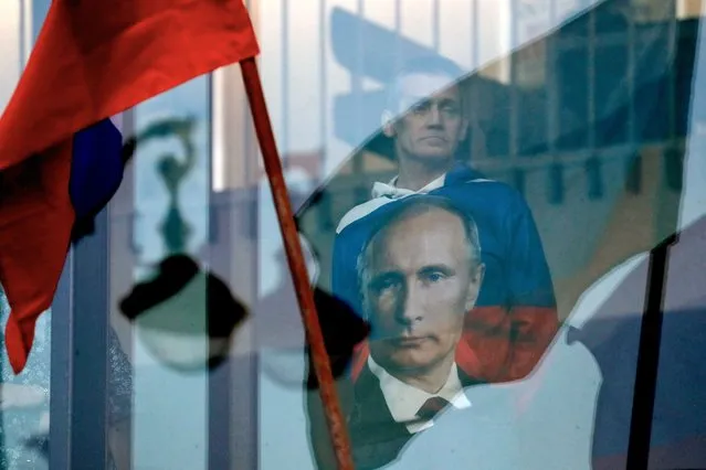 A man wearing a shirt with an image of Russian President Vladimir Putin looks through a window as police guard the area around the Oktyabrsky Concert Hall, amid heightened security measures, prior to the concert of the rock group “Picnic” in St. Petersburg, Russia, 27 March 2024. (Photo by Anatoly Maltsev/EPA/EFE)