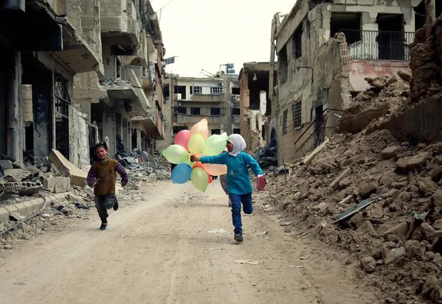 Syrian children run with balloons past heavily damaged buildings in the neighbourhood of Jobar, on the eastern outskirts of the Syrian capital Damascus on April 9, 2016. (Photo by Amer Almohibany/AFP Photo)