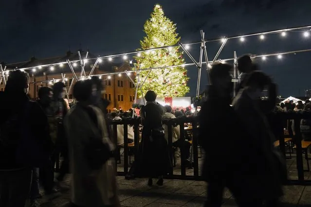 People wearing a face mask, walk past a Christmas tree, at a shopping mall in Yokohama, near Tokyo, Saturday, December 25, 2021. (Photo by Shuji Kajiyama/AP Photo)