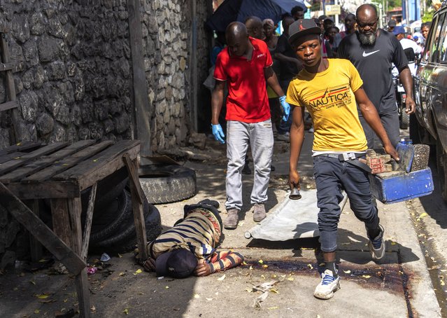 A shoeshiner walks past a bloodied body being removed by forensic workers in Port-au-Prince, Haiti, Wednesday, May 1, 2024. Forensics said the body had gunshot wounds. (Photo by Ramon Espinosa/AP Photo)