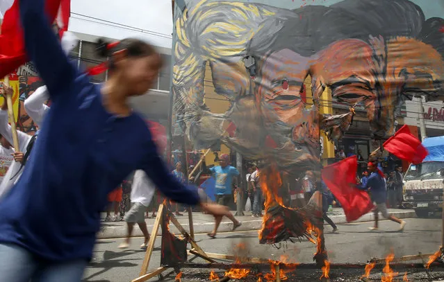Protesters dance around the burning giant mural of, from left, U.S. President Donald Trump, Philippines President Rodrigo Duterte and Chinese President Xi Jinping during a short program to coincide with the 4th State of the Nation (SONA) address by Duterte Monday, July 22, 2019 in suburban Quezon city, northeast of Manila, Philippines. Duterte is facing criticisms about his alleged closeness with China as well as the thousands of killings in his so-called war on drugs. (Photo by Bullit Marquez/AP Photo)
