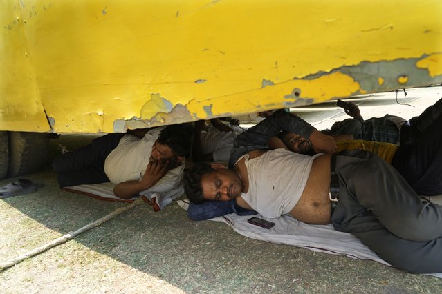 Election officers rest beneath a parked bus on a hot summer day before proceeding to their allotted polling stations on the eve of the sixth round of multi-phase national elections in Prayagraj, Uttar Pradesh, India, Friday, May 24, 2024. Parts of northwest India are sweltering under scorching temperatures with the capital New Delhi under a severe weather alert as extreme temperatures strike parts of the country. (Photo by Rajesh Kumar Singh/AP Photo)