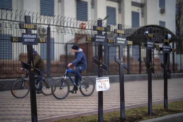 Cyclists ride past an installation of crosses on which is written “Russian occupier”, in front of the Russian Embassy in Kyiv, Ukraine, Wednesday, February 23, 2022. Ukraine urged its citizens to leave Russia as Europe braced for further confrontation Wednesday after Russia's leader received authorization to use military force outside his country and the West responded with a raft of sanctions. (Photo by Emilio Morenatti/AP Photo)