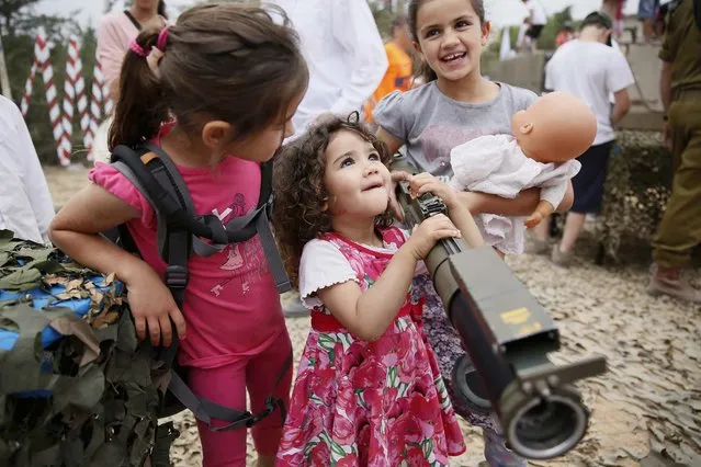 An Israeli child holds a rocket launcher as another holds her doll during a traditional military weapon display to mark the 66th anniversary of Israel's Independence at the West Bank settlement of Efrat on May 6, 2014 near the biblical city of Bethlehem. Israelis are marking Independence Day, celebrating the 66th year since the founding of the Jewish State in 1948 according to the Jewish calendar. (Photo by Gali Tibbon/AFP Photo)