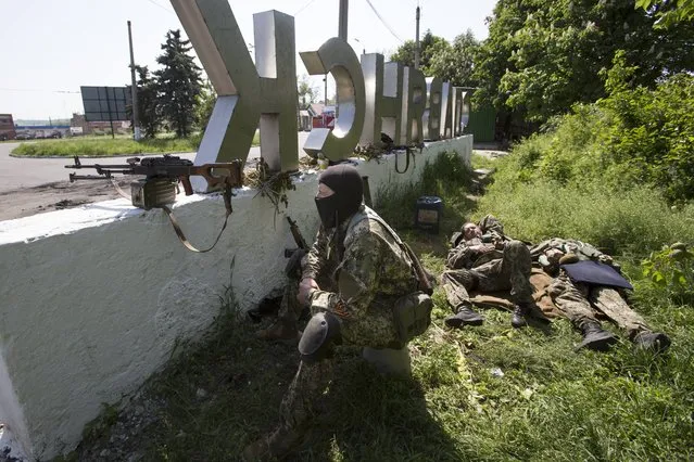 Pro-Russian gunmen take their position behind a sign with the word “Slovyansk”,  at a checkpoint blocking the major highway which links Kharkiv, outside Slovyansk, eastern Ukraine, Friday, May 16, 2014. (Photo by Alexander Zemlianichenko/AP Photo)