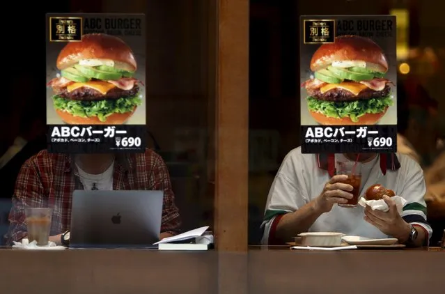 Customers sitting inside a fast food shop are seen behind its hamburger advertisement poster on a window at the Tokyo's Akihabara shopping district, Japan, May 19, 2015. (Photo by Yuya Shino/Reuters)