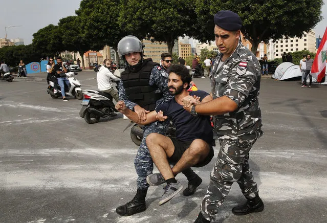 Riot police remove an anti-government protester blocking a main highway with his body in Beirut, Lebanon, Saturday, October 26, 2019. The removal of the roadblocks on Saturday comes on the tenth day of protests in which protesters have called for civil disobedience until the government steps down. (Photo by Hussein Malla/AP Photo)