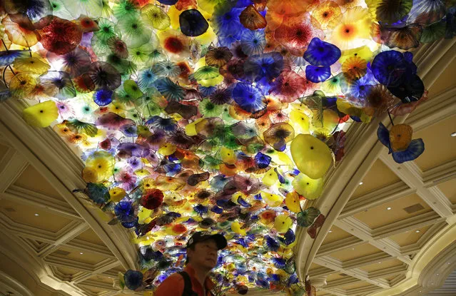 In this May 31, 2017, photo, a man stands beneath an installation by artist Dale Chihuly titled, “Fiori di Como”, (Flowers of Como), suspended from the ceiling of the lobby at the Bellagio hotel and casino in Las Vegas. Chihuly, who began working with glass in the 1960s, is a pioneer of the glass art movement. Known for styles that include vibrant seashell-like shapes, baskets, chandeliers and ambitious installations that can be seen in botanical gardens, hotels and the new Chihuly Sanctuary at the Buffett Cancer Center in Omaha, Neb. (Photo by John Locher/AP Photo)