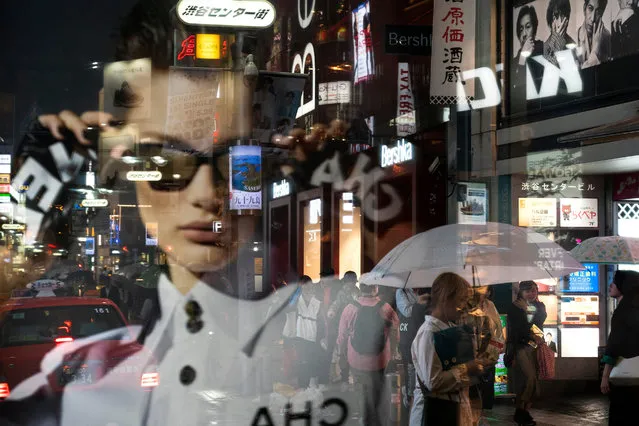 Pedestrians are seen through the reflection of an advertisement in a window as they walk along a busy street in the Shibuya district of Tokyo on June 9, 2019. (Photo by Jae C. Hong/AP Photo)