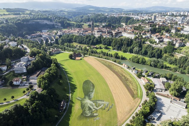 A picture taken with a drone shows a giant biodegradable land art painting titled “Bridges?” by French-Swiss artist Saype to celebrate 125th anniversary of Fribourg Tourism at the foot of the Poya Bridge, in the city of Fribourg, Switzerland, 16 August 2024. The fresco, depicting a child building a bridge with small wooden blocks, was created using environmentally friendly paint consisting of biodegradable pigments made from charcoal, chalk, water and milk proteins. (Photo by Cyril Zingaro/EPA/EFE)