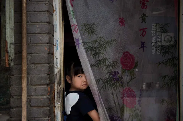 A girl looks out from the doorstep of her house in Beijing on June 9, 2016. (Photo by Nicolas Asfouri/AFP Photo)