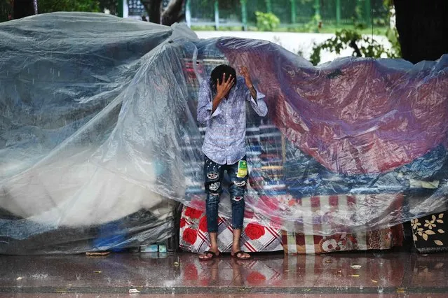 A man tries to protect himself from rain while standing along a street in New Delhi on July 16, 2022. (Photo by Sajjad Hussain/AFP Photo)