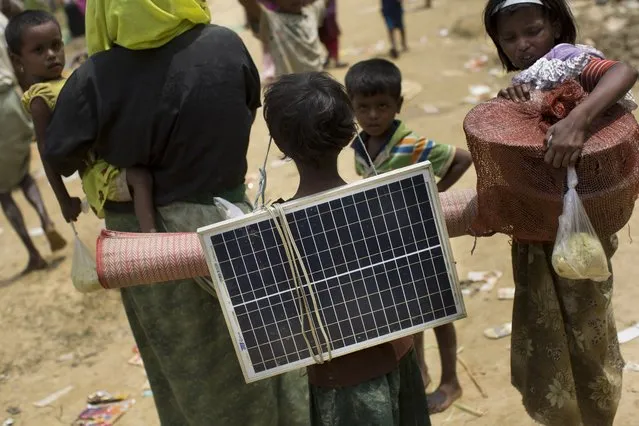 In this Thursday, September 7, 2017, photo, a Rohingya Muslim child carries a solar panel as she crosses over the border from Myanmar into Bangladesh in Teknaf area. Cellphones to reach out to separated relatives, bags of spices that remind them of home and solar panels to bring a little light to their ragged tents are some of the things the exhausted Rohingya Muslims carry with them as they escape the violence that they’ve endured in Myanmar’s Rakhine state over the last two weeks. (Photo by Bernat Armangue/AP Photo)