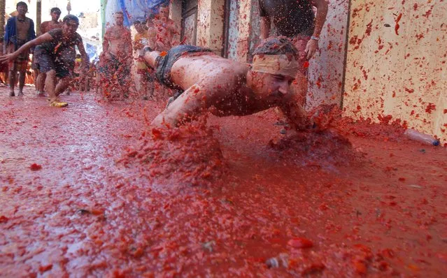 A man dives into a puddle of squashed tomatoes,  during the annual “Tomatina” tomato fight fiesta in the village of Bunol, 50 kilometers outside Valencia, Spain, Wednesday, August 27, 2014. (Photo by Alberto Saiz/AP Photo)
