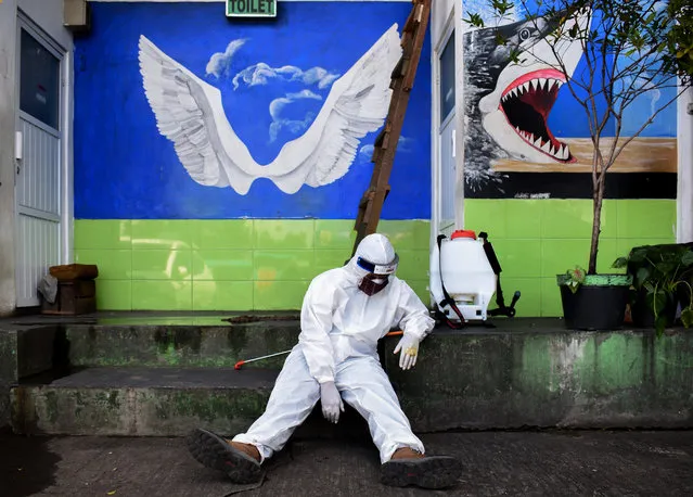 A health agency official, seen alongside his disinfectant dispenser, rests by the entrance to a public toilet as other colleagues (not pictured) conduct polymerase chain reaction (PCR) testing for the COVID-19 coronavirus at a bus station in Bandung, West Java, on May 13, 2020. (Photo by Timur Matahari/AFP Photo)