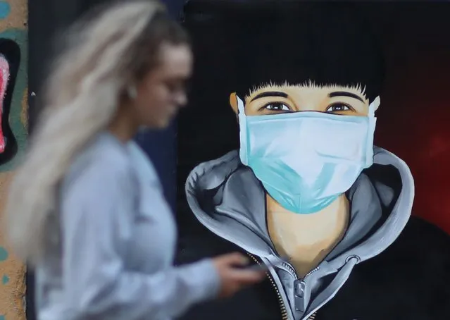 A woman checks her mobile phone as she walks past a mural depicting a man wearing a face mask,as the spread of the coronavirus disease (COVID-19) continues, in Sale, Britain, April 11, 2020. (Photo by Phil Noble/Reuters)