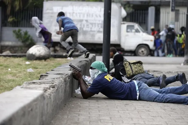 Armed off-duty police officers take cover during and exchange of gunfire with army soldiers during a protest over police pay and working conditions, in Port-au-Prince, Haiti, Sunday, February 23, 2020. (Photo by Dieu Nalio Chery/AP Photo)