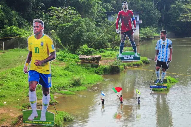 Fans wave flags next to the giant cutouts of players from Brazil's Neymar (L), Portuguese Cristiano Ronaldo (C) and Argentine Lionel Messi, erected by football fans in river Cherupuzha at Kozhikode in India's Kerala state on November 7, 2022, ahead of the Qatar 2022 FIFA World Cup football tournament. (Photo by AFP Photo/Stringer)