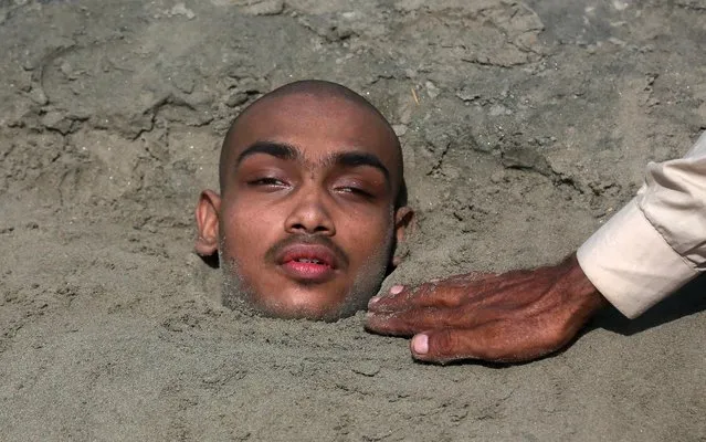 A Pakistani adjusts sand around an ailing child partially buried up to his neck at seaside during the partial solar eclipse in Karachi, Pakistan, Sunday, June 21, 2020. Superstitious people hope that burying ailing persons during a solar eclipse will assist in curing them. (Photo by Fareed Khan/AP Photo)