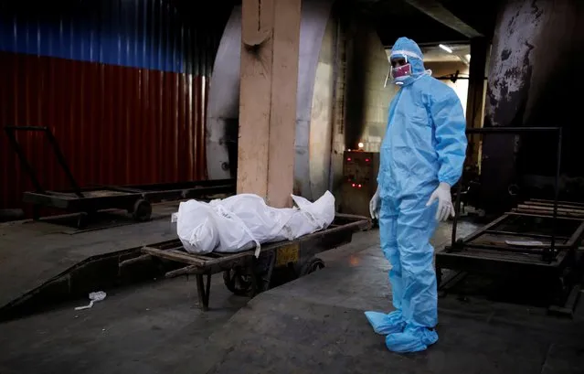 A relative wearing personal protective equipment (PPE) stands next to a body of a man who died due to the coronavirus disease (COVID-19), before his cremation at a crematorium in New Delhi, India on August 22, 2020. (Photo by Adnan Abidi/Reuters)