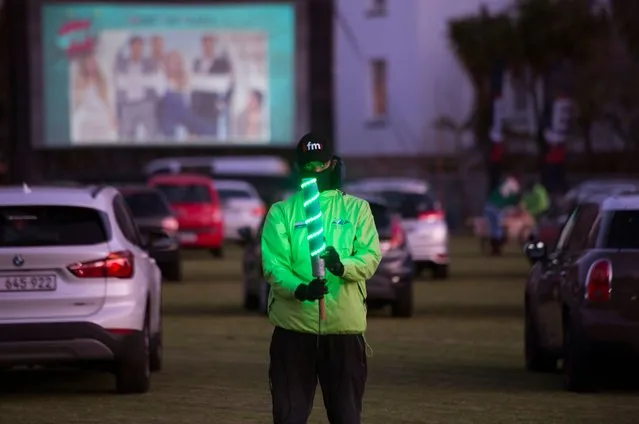 A park attendant helps people to park their cars in the right position at the Galileo drive-in, being held on a school sports field in Cape Town, on August 26, 2020. Drive-in cinemas have largely gone out of fashion, but with the Covid-19 pandemic affecting the country, this drive-in has been a way for people to safely go out and watch movies. (Photo by Rodger Bosch/AFP Photo)