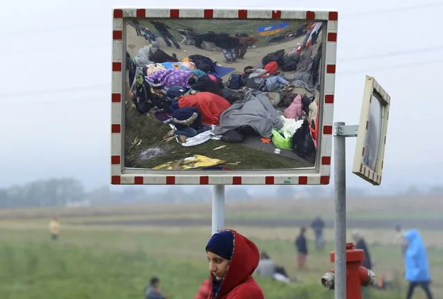 A girl looks on as resting migrants are seen in a street mirror after crossing the border from Croatia in Rigonce, Slovenia October 21, 2015. The Slovenian parliament passed legislation early on Wednesday that will give the army more power to help police guarding the state border as thousands of migrants flood into the country from Croatia after Hungary sealed off its border. (Photo by Antonio Bronic/Reuters)