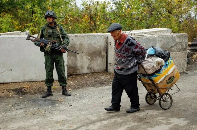 A man carries his belongings past a member of the self-proclaimed Luhansk People's Republic forces on a road located on the troops contact line between pro-Moscow rebels and Ukrainian troops, in the settlement of Stanytsia Luhanska in Luhansk region, Ukraine, October 9, 2016. (Photo by Alexander Ermochenko/Reuters)
