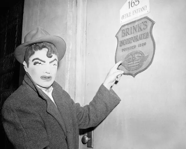 A newsman wears a rubber mask similar to that worn by seven bandits who robbed Brink's armored car firm in Boston of $1, 50,000, January 18, 1950. The reporter points to name plate on first of six locked doors opened by the gunmen. Mask was one of several purchased in joke shops by newsmen and police to see if they resembled description given by Brink's employees. (Photo by AP Photo)