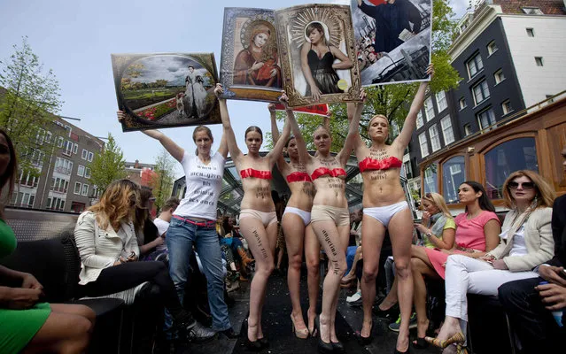 Dutch artist Alice Wielinga wears a white t-shirt next to nearly nude models as they all hold up stereotypical depictions of women to protest for women's rights during Amsterdam Floating fashion week in Amsterdam, the Netherlands, on May 29, 2013. (Photo by Cris Toala Olivares/Reuters)