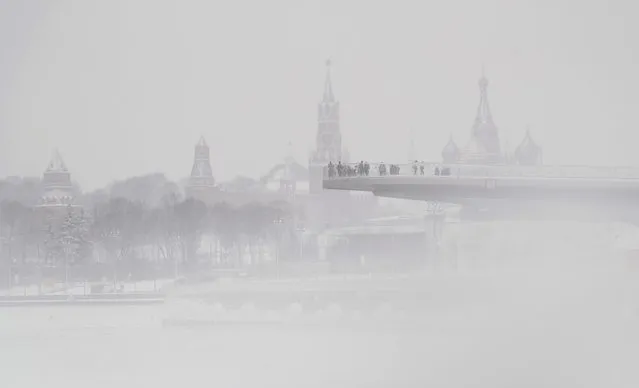 People walk on the floating bridge at the Zaryadye park next to the Spasskaya tower of the Moscow Kremlin and the St. Basil Cath​edral during a snowfall day in Moscow, Russia, 02 January 2021. (Photo by Maxim Shipenkov/EPA/EFE)