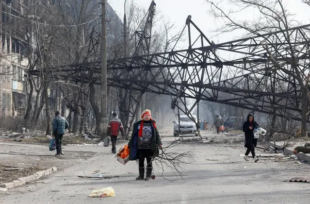 Local residents walk near a fallen electricity pylon and an apartment building destroyed in the course of Ukraine-Russia conflict in the besieged southern port city of Mariupol, Ukraine on March 25, 2022. (Photo by Alexander Ermochenko/Reuters)